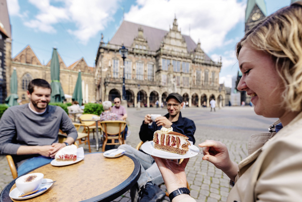 Drei Personen sitzen an einem Tisch beim Kuchenessen auf dem Bremer Marktplatz.